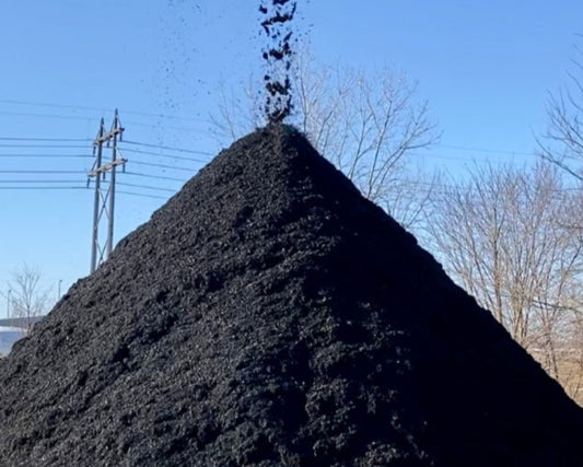 Premium dyed black mulch in a large pile coming off a conveyor at Raney Tree Care facility in Moline, IL