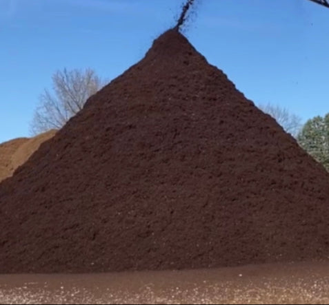 Premium dyed brown mulch in a large pile coming off a conveyor at Raney Tree Care facility in Moline, IL