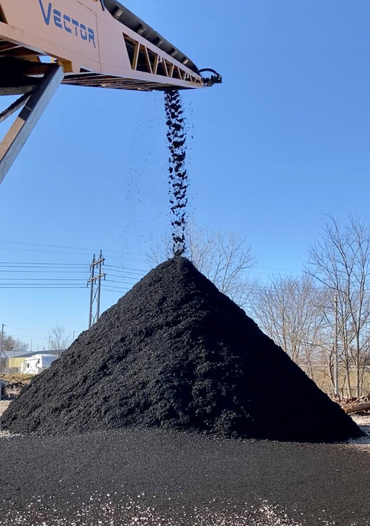Premium dyed black mulch in a large pile coming off a conveyor at Raney Tree Care facility in Moline, IL