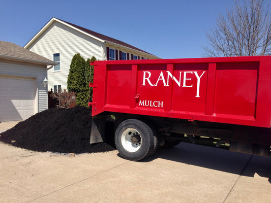 Raney delivery truck parked in a driveway, delivering a fresh pile of black mulch at a customer's home in the Quad City Area.
